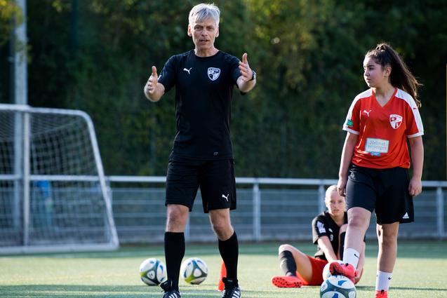 Trainer erklärt Technik beim Fußballtraining, während Spielerinnen auf dem Kunstrasen stehen und sitzen.