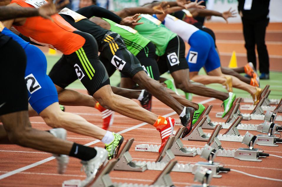 Start einer Sprintveranstaltung mit mehreren Athleten in Blockstartposition auf einer Laufbahn.