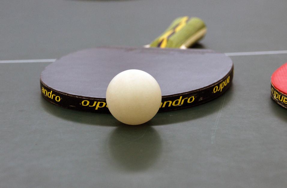 Nahaufnahme eines Tischtennisschlägers mit weißem Ball auf einer grünen Tischtennisplatte.